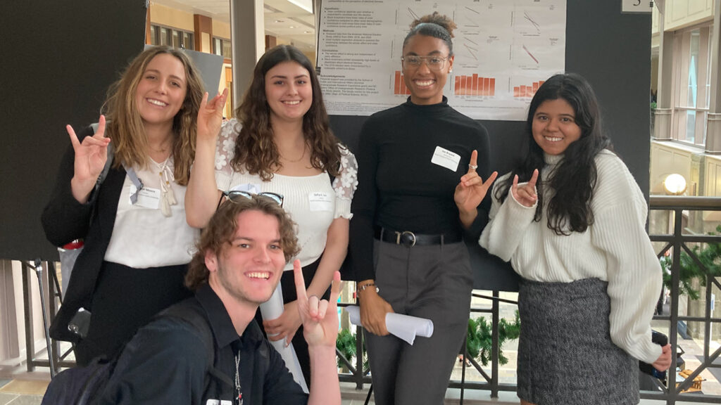 Students pose next to a research poster